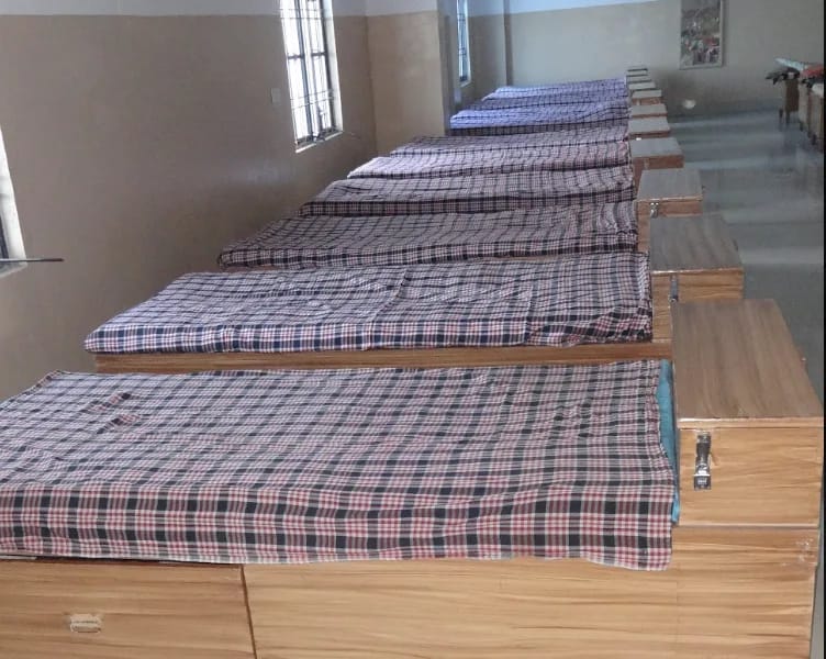 A row of neatly made beds with wooden storage trunks in the dormitory